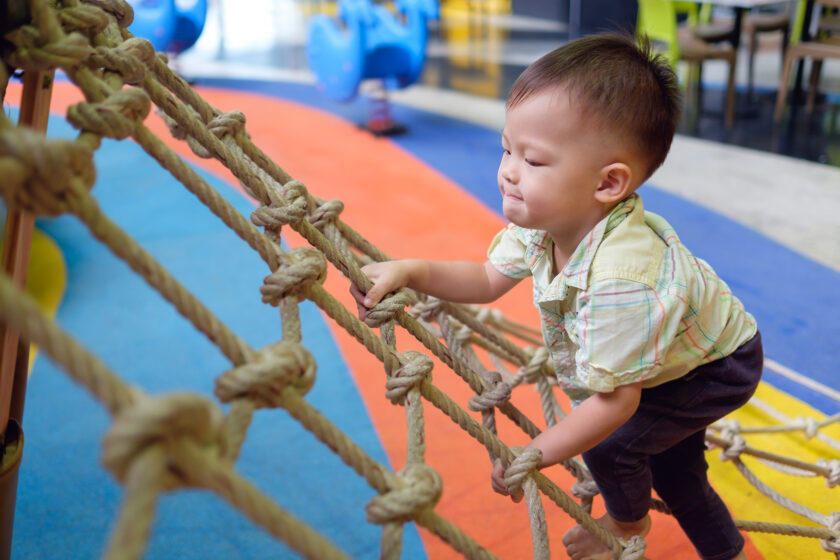 A young boy climbing on a rope in a playground.